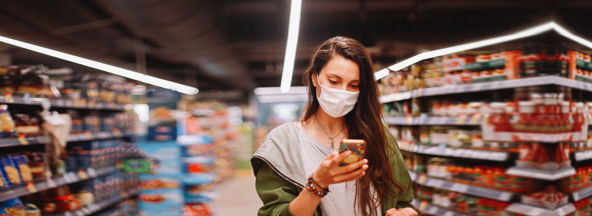 Mujer con mascarilla de compras con su celular en el supermercado