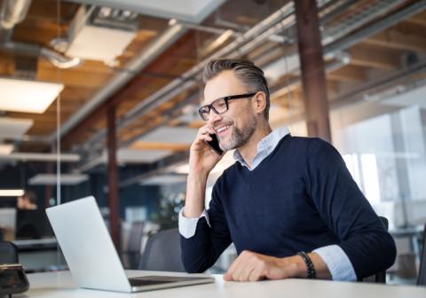 Persona hablando por teléfono frente a la laptop