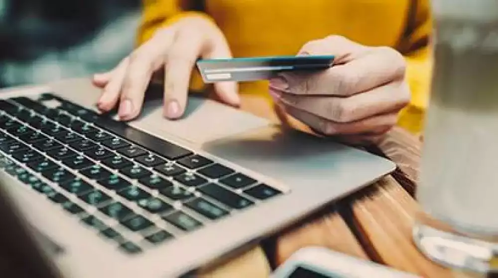 Persona escribiendo en computadora con tarjeta en mano