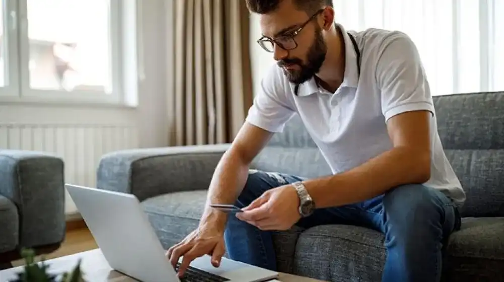 Joven usando computadora con una tarjeta de crédito