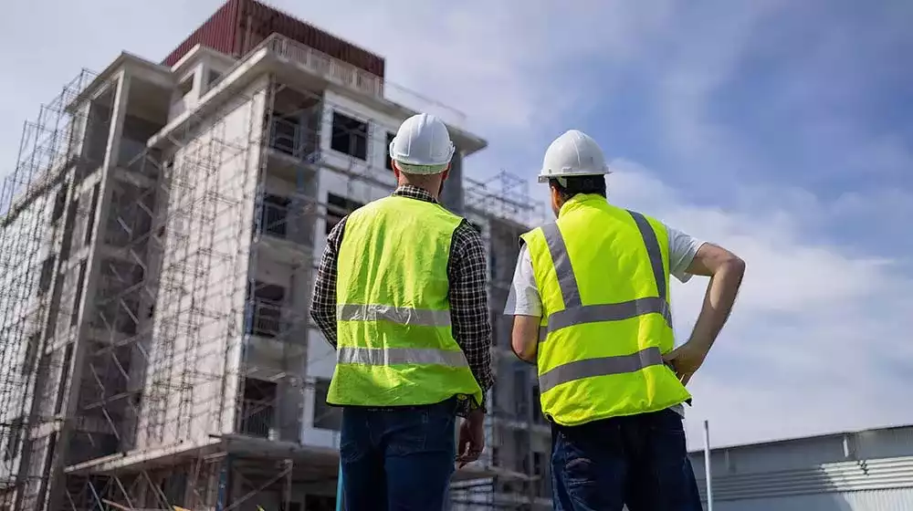 Dos personas con casco y chaleco de seguridad viendo  una construccion