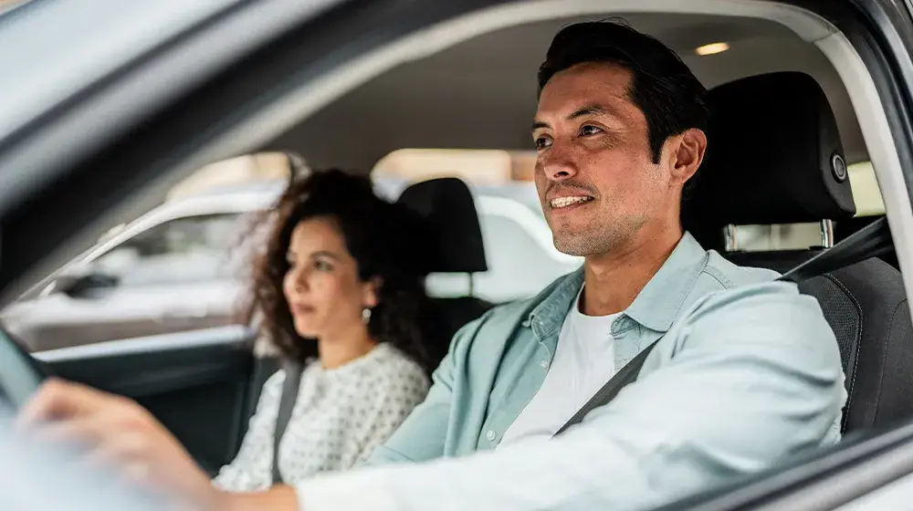 Persona y su acompañante conduciendo con su sticker Compass para evvitar tiquetes, filas y efectivo en estacionamientos