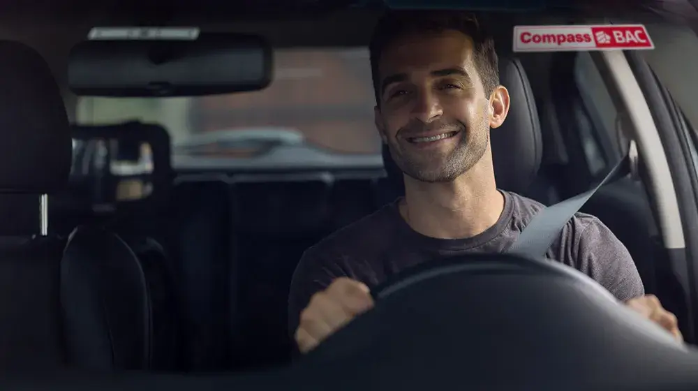 Persona sonriente al ver su sticker de Compass BAC sobre el parabrisas