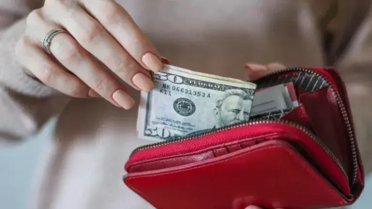 Manos de mujer sacando unos billetes de 50 dólares de su billetera roja